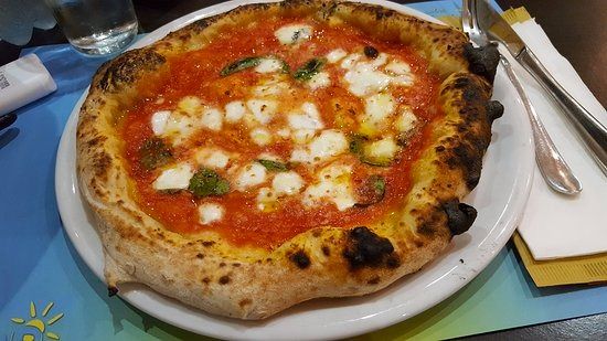 A margherita on a board in front of a wood-fired oven.